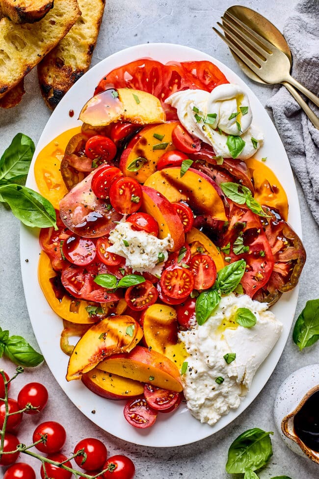 tomato peach burrata salad on platter with fresh basil and balsamic glaze.