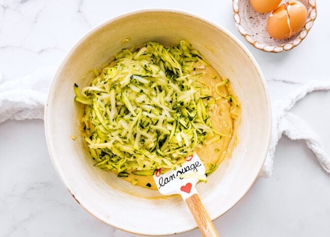 lime zucchini loaf cake batter in bowl with spatula. 