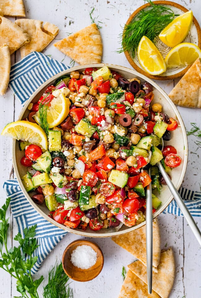 Greek chickpea salad in bowl with serving utensils. 