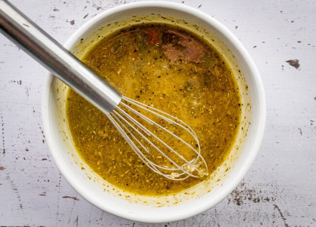 Greek chickpea salad dressing in bowl with whisk. 