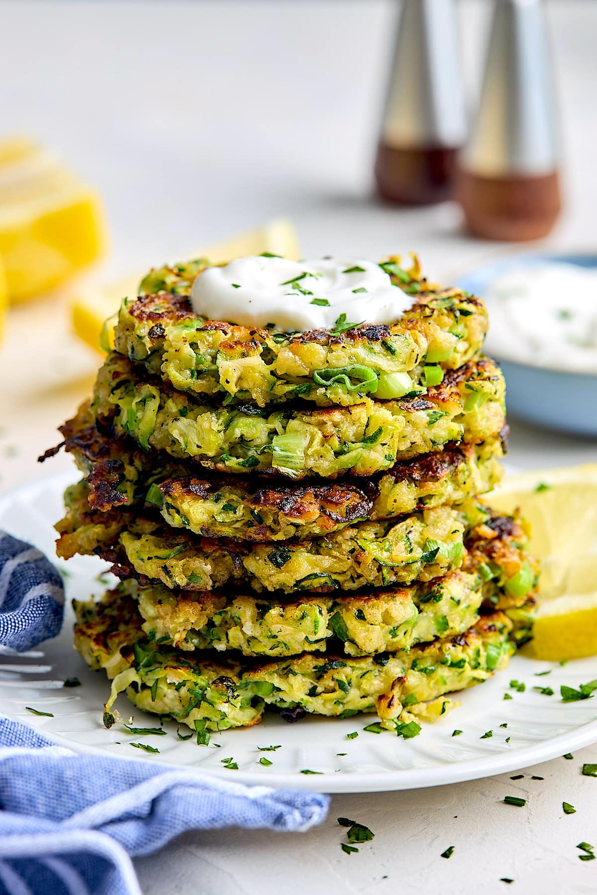 stack of zucchini fritters with sour cream on top on plate. 