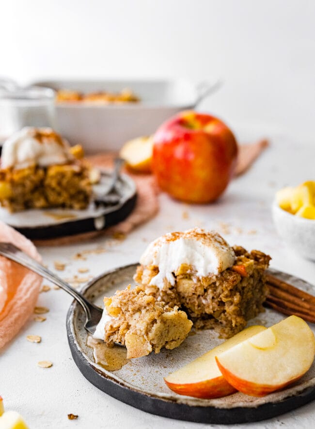 apple cinnamon baked oatmeal on plate with whipped cream and apple slices. 