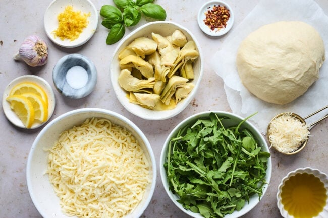 lemon artichoke arugula pizza ingredients in bowls.