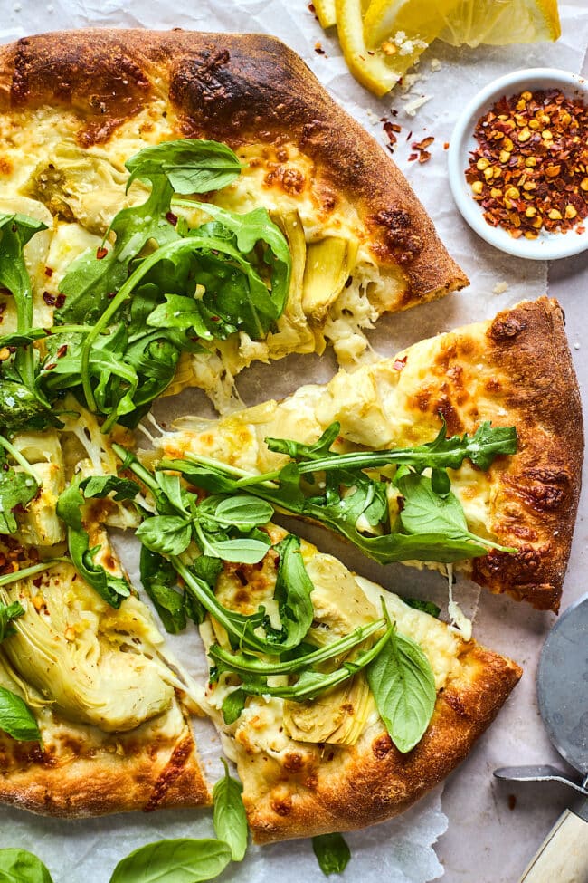 lemon artichoke arugula pizza cut in slices with crushed red pepper flakes.