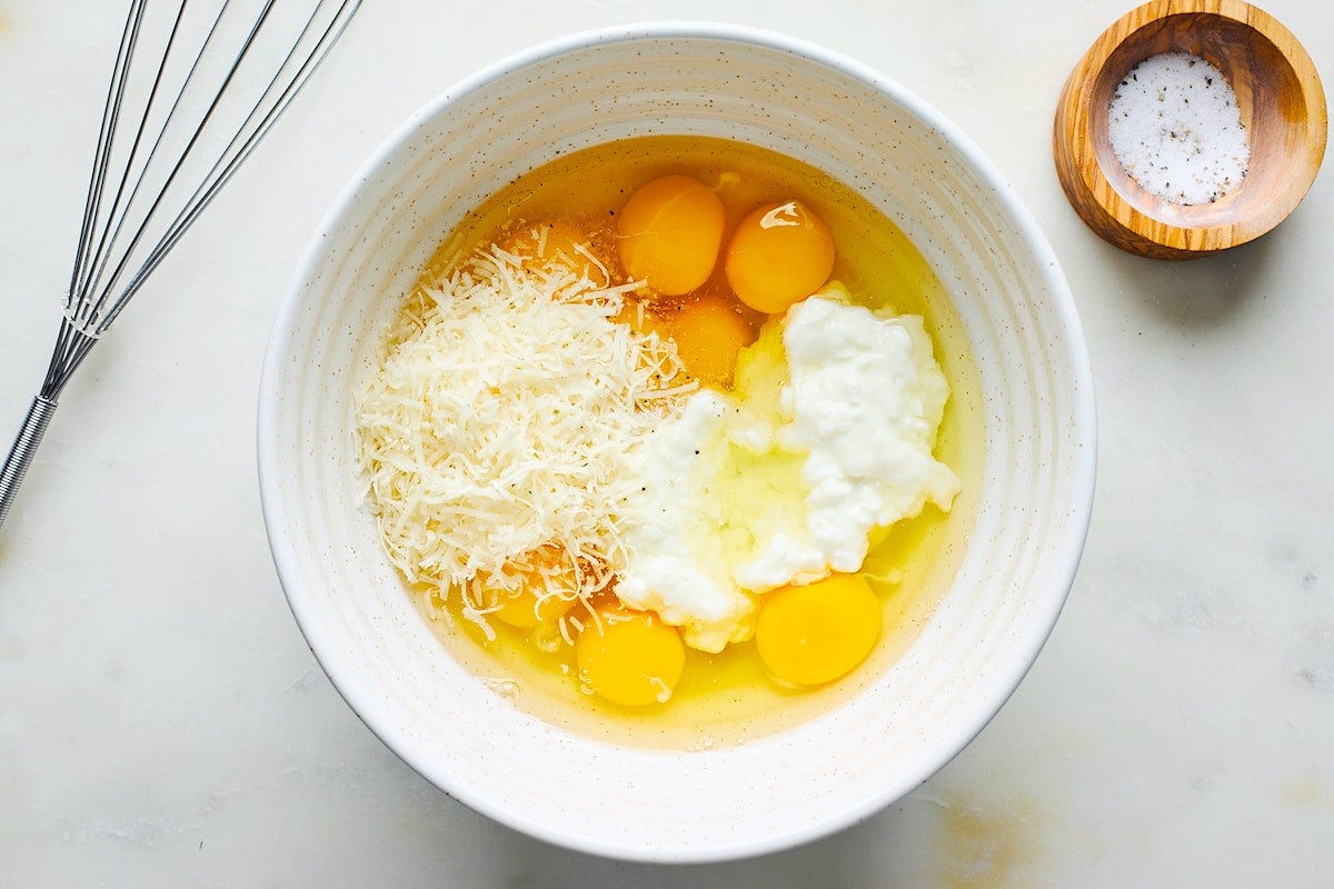 cottage cheese, eggs, and parmesan cheese in mixing bowl with whisk and small wood bowl with salt. 