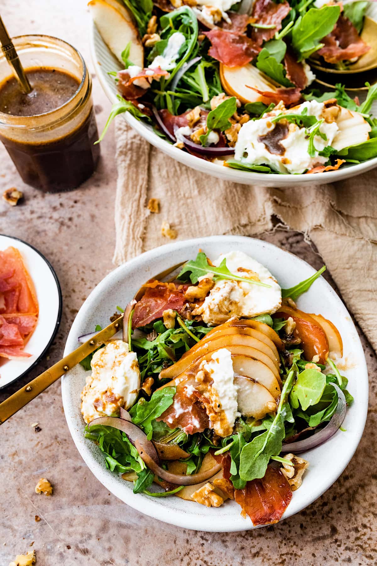 crispy prosciutto salad on plate with pears, burrata, red onions, walnuts, balsamic vinaigrette, and a fork. 