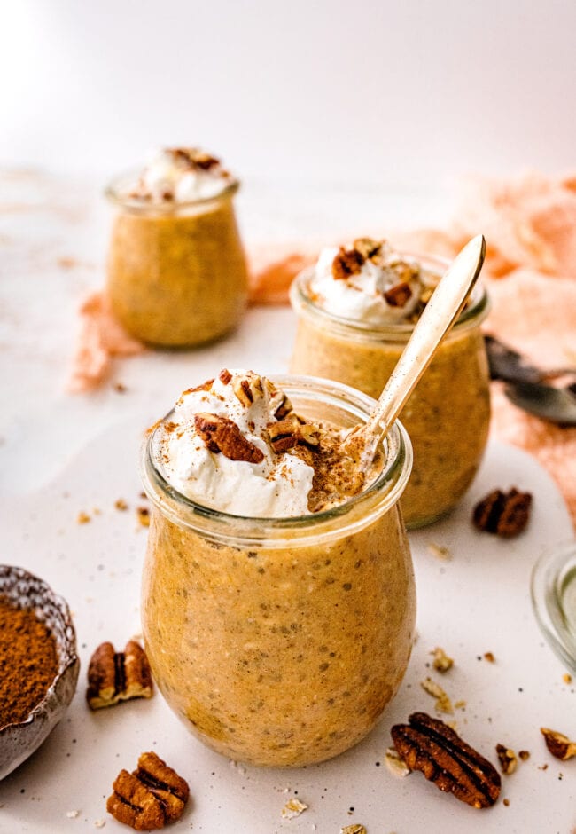 pumpkin overnight oats with whipped cream and pecans in jars.