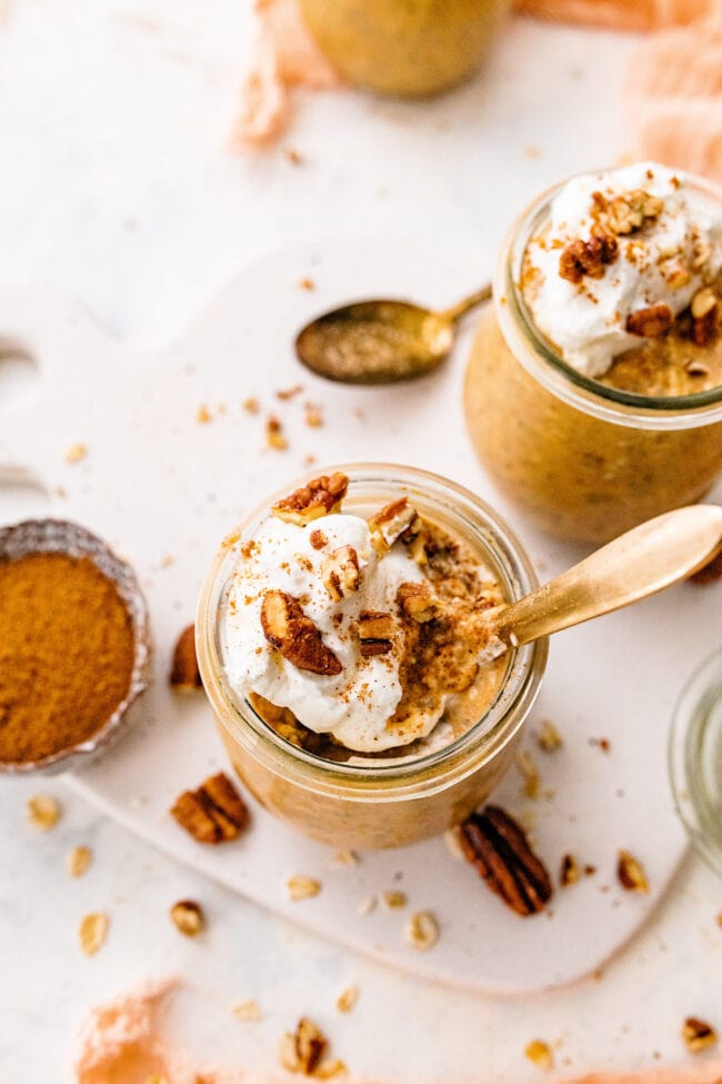 pumpkin overnight oats in jar with whipped cream, pecans, cinnamon, and spoon.