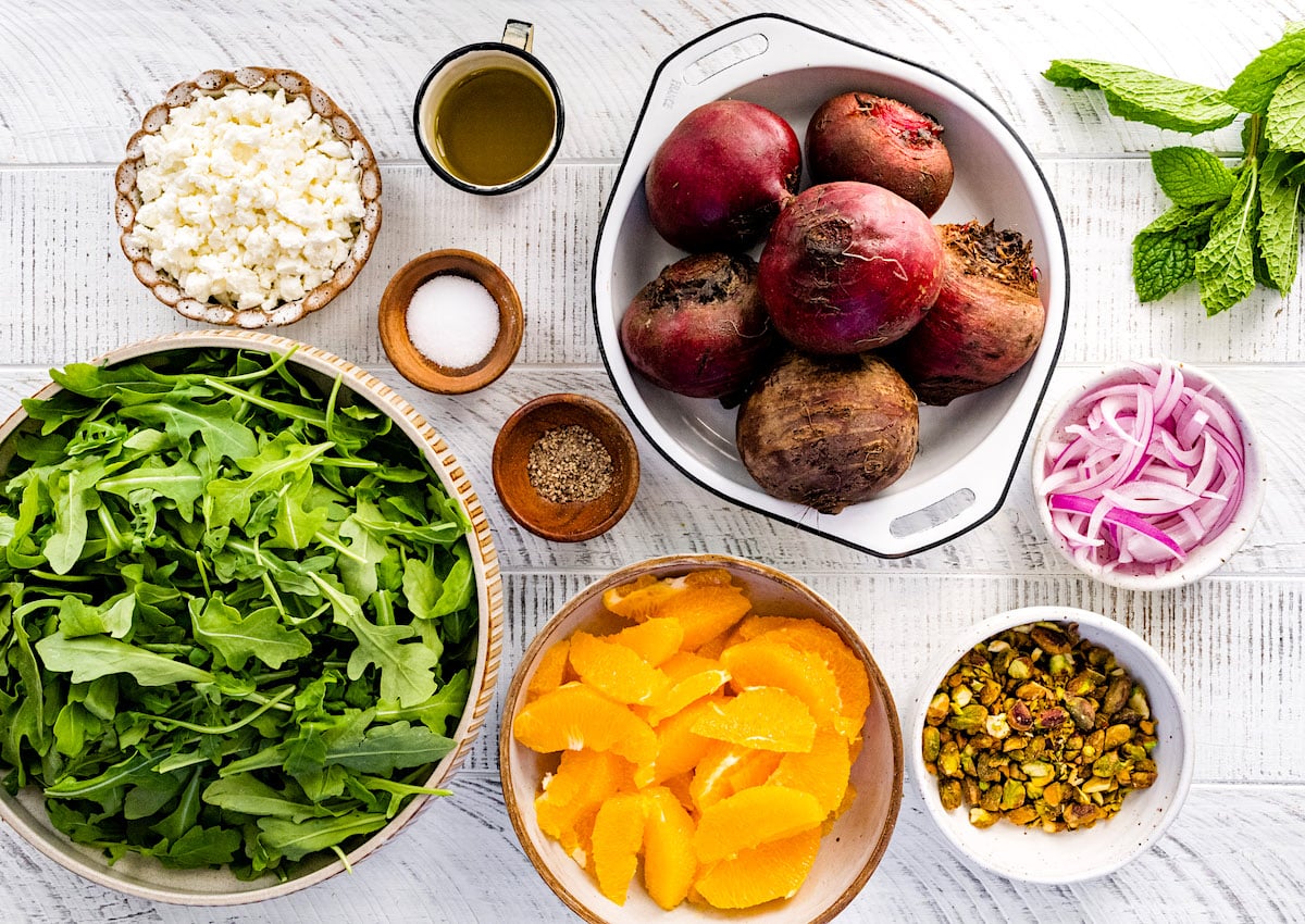 arugula, orange slices, pistachios, red onions, beets, and goat cheese in bowls. 