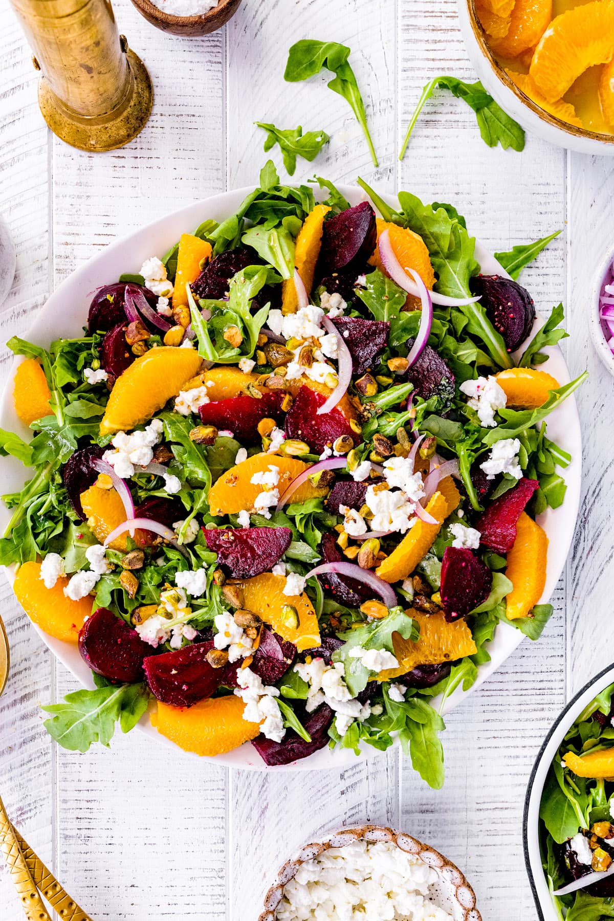 arugula in bowl with roasted beets, orange slices, red onion, goat cheese, and pistachios.