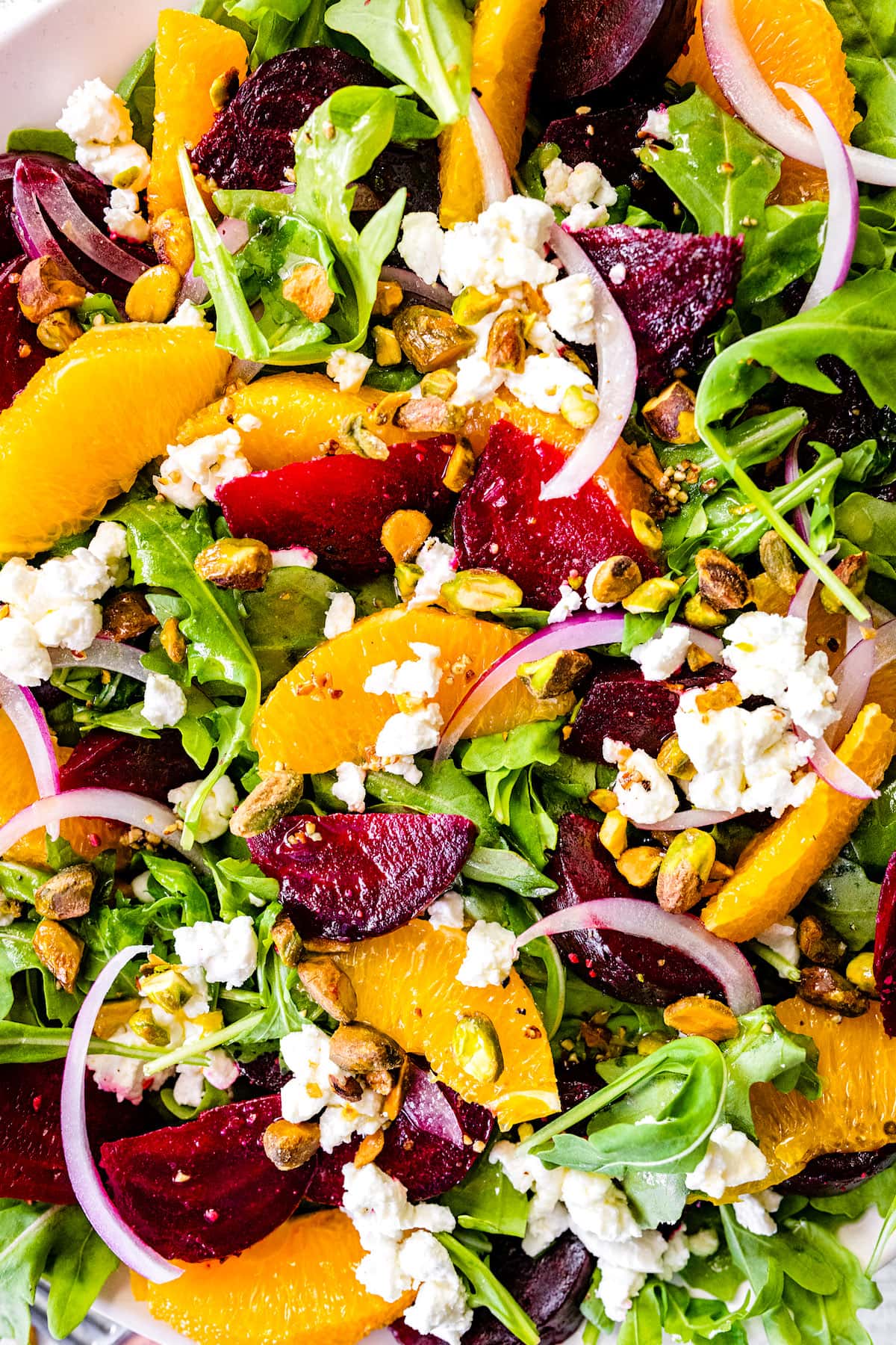 close up shot of beet salad with arugula, beets, orange slices, goat cheese, red onion, and pistachios.