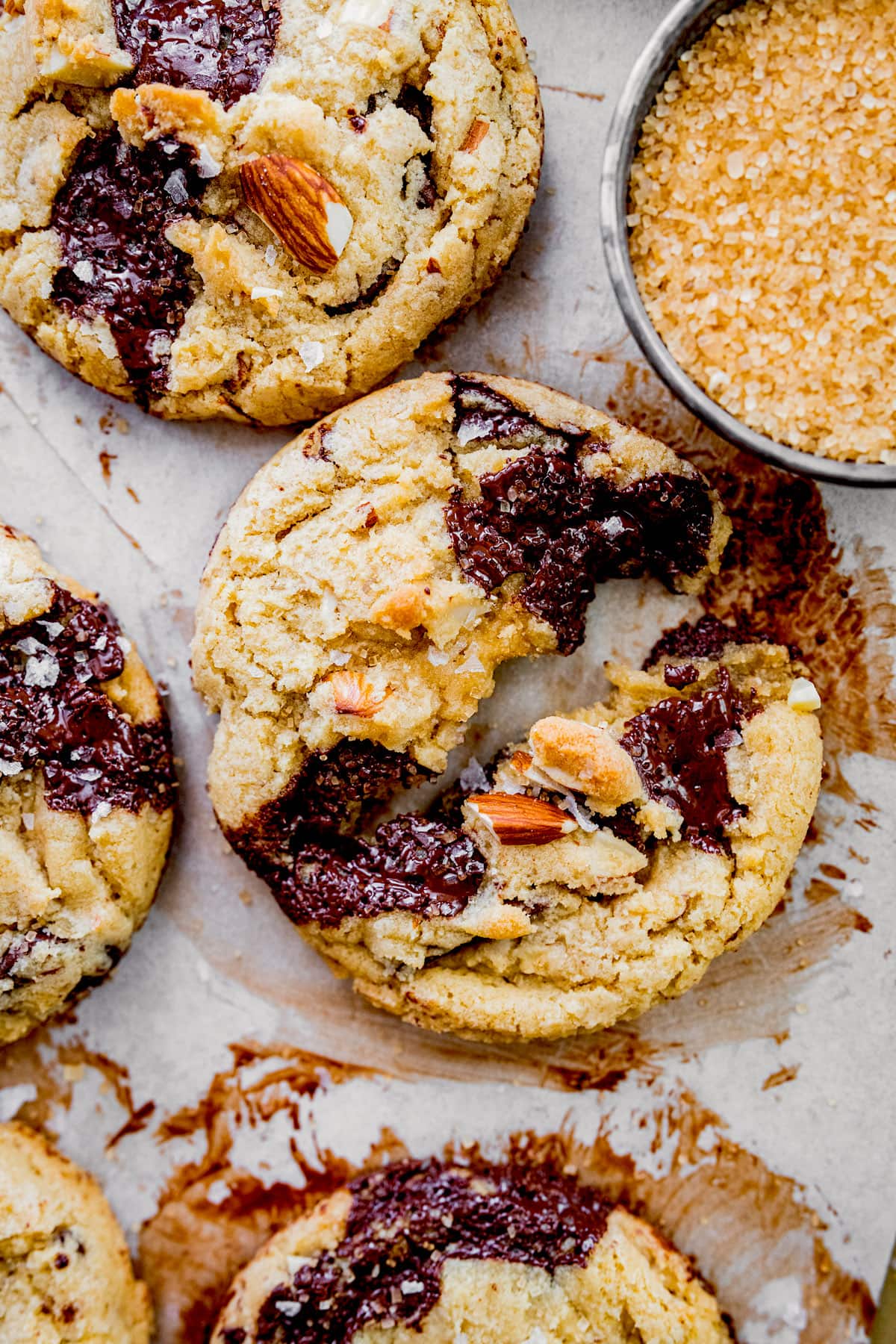 almond chocolate chip cookie broken in half with turbinado sugar on parchment paper.