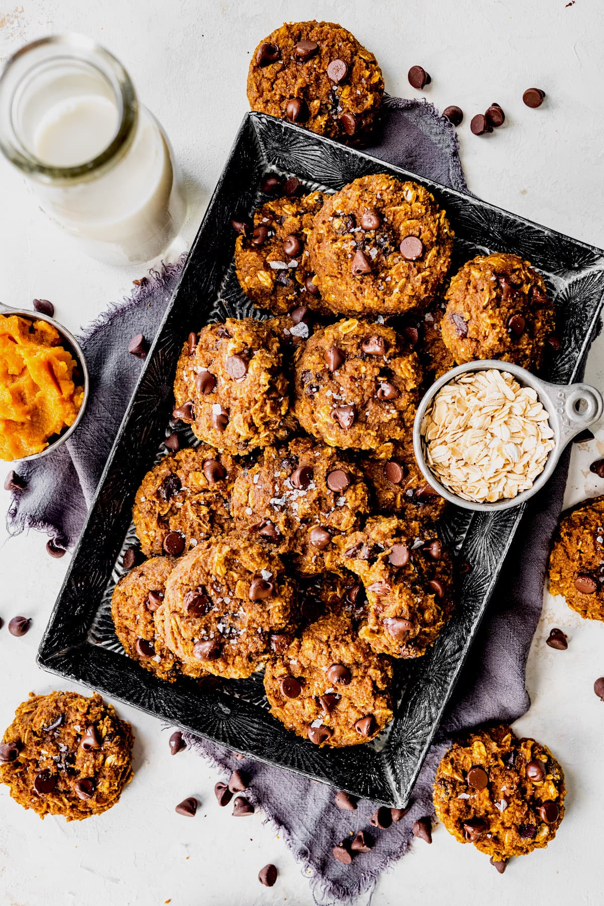 pumpkin breakfast cookies in pan with oatmeal and chocolate chips with a jar of milk. 