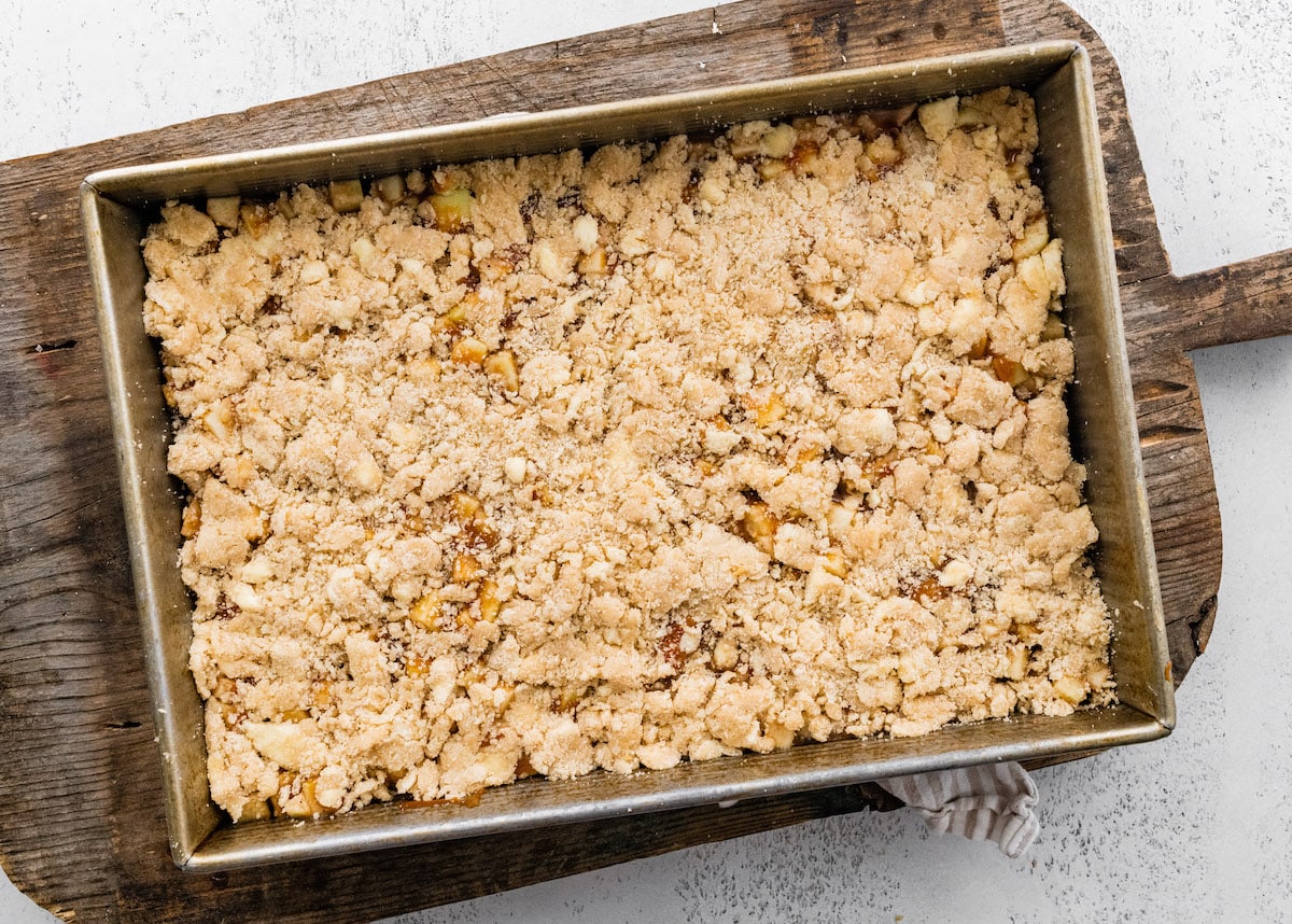 unbaked salted caramel apple pie bars with crumb topping in a 9x13-inch pan. 