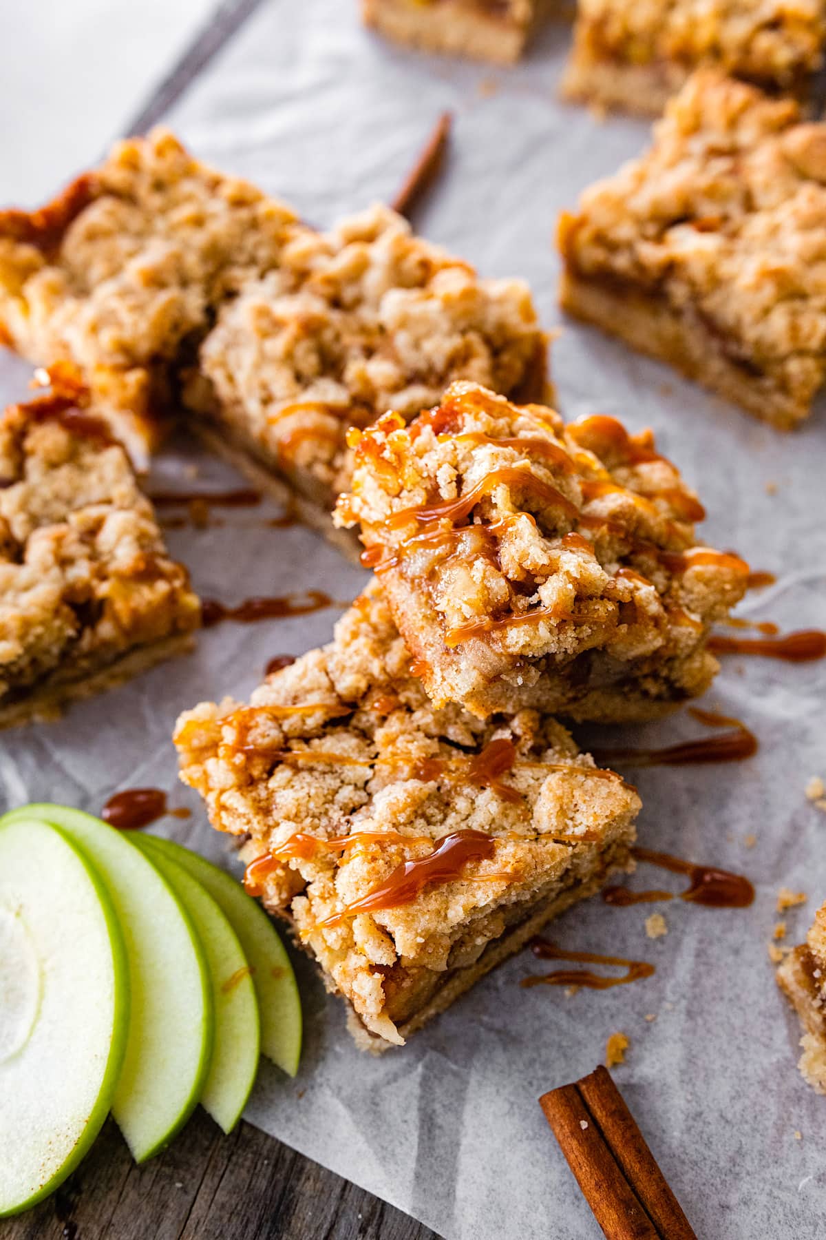 salted caramel apple crumb bars cut in squares with a drizzle of salted caramel sauce on parchment paper.