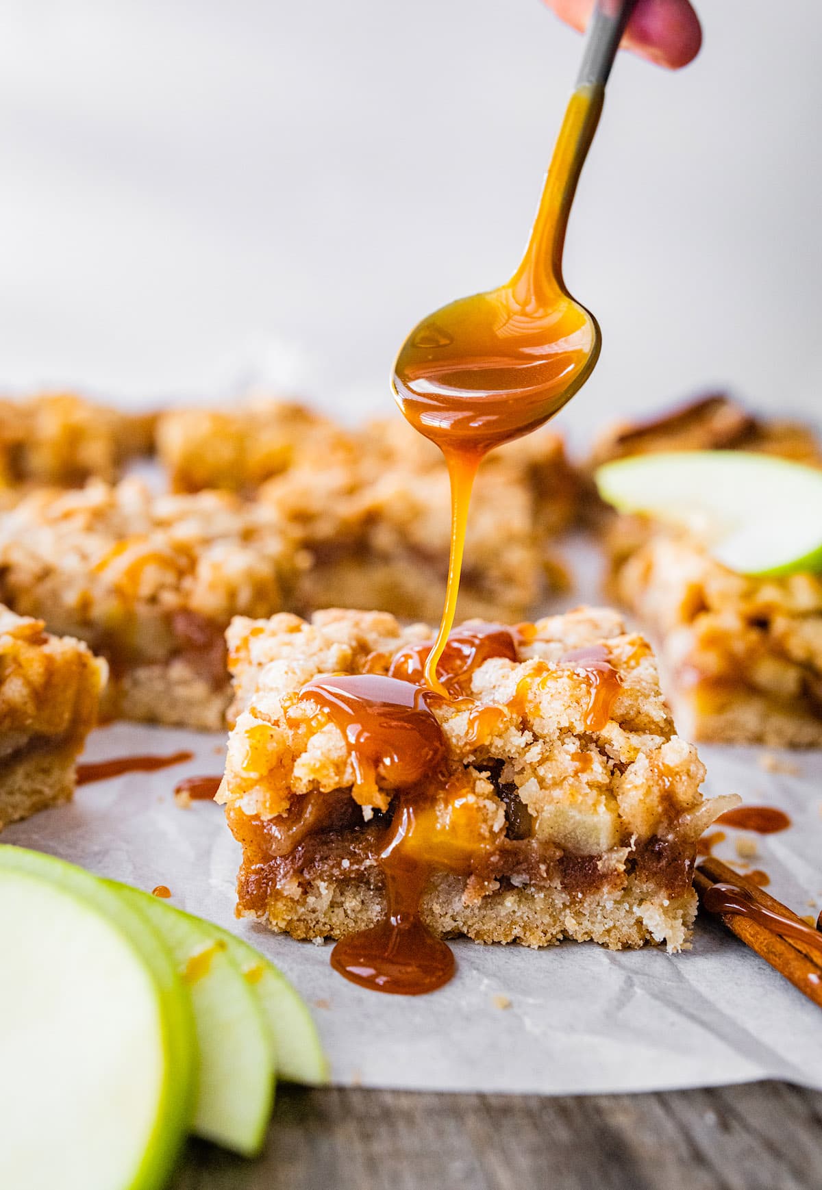 salted caramel apple crumb bars cut in squares with a drizzle of salted caramel sauce on top from a spoon.