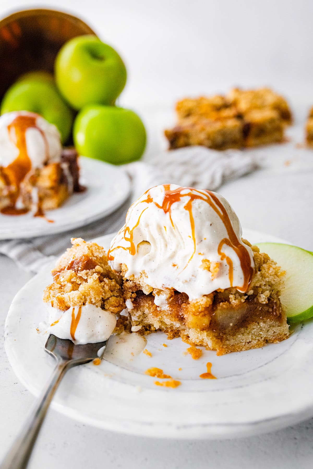salted caramel apple crumb bar topped with vanilla ice cream and salted caramel sauce on plate with fork.