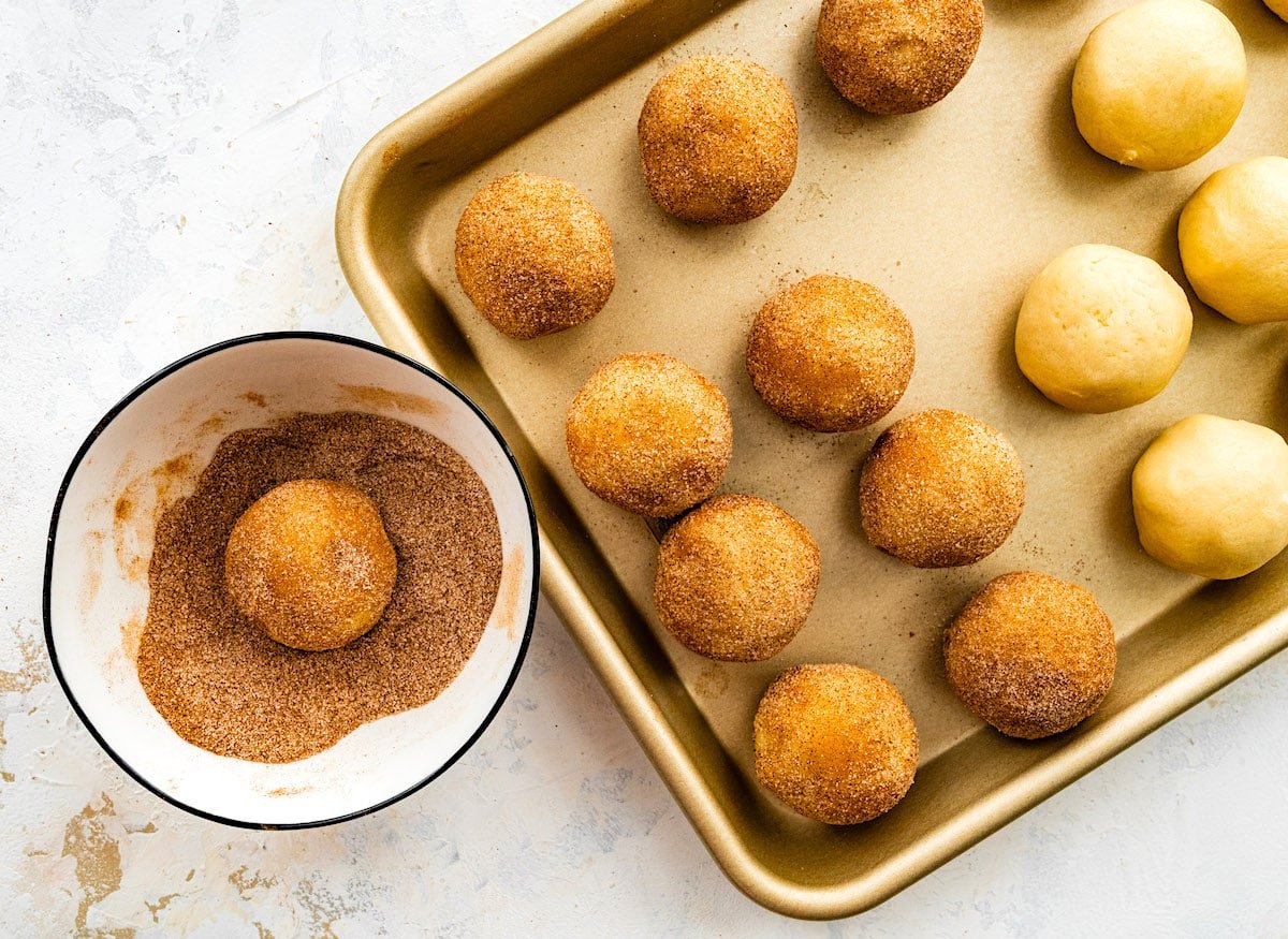 snickerdoodle cookie dough balls on baking sheet rolled in cinnamon sugar.