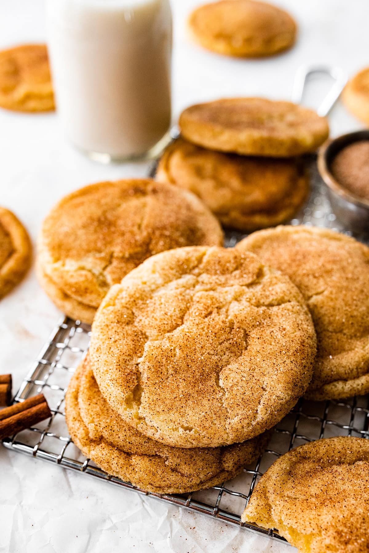 snickerdoodle cookies on cooling rack with cinnamon sticks and glass bottle of milk. 