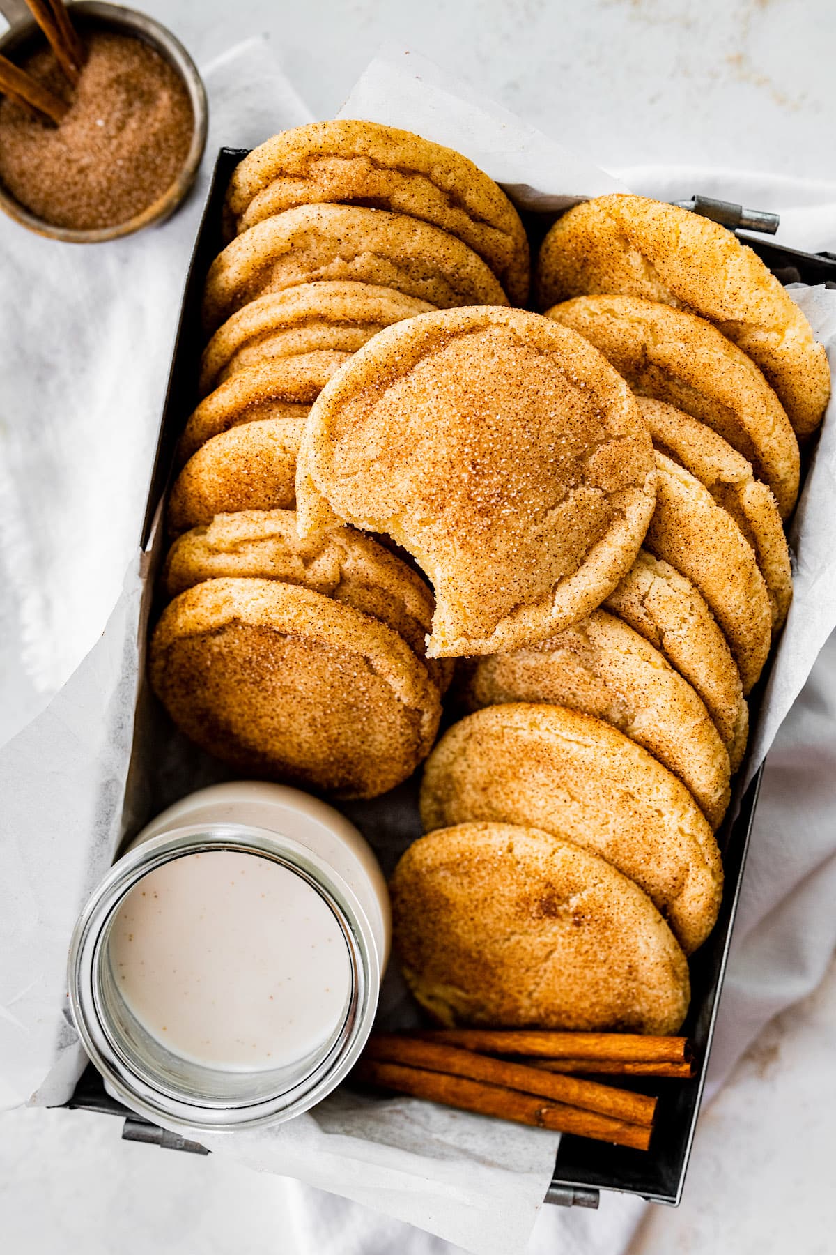 snickerdoodle cookies in box with parchment paper and glass of milk.