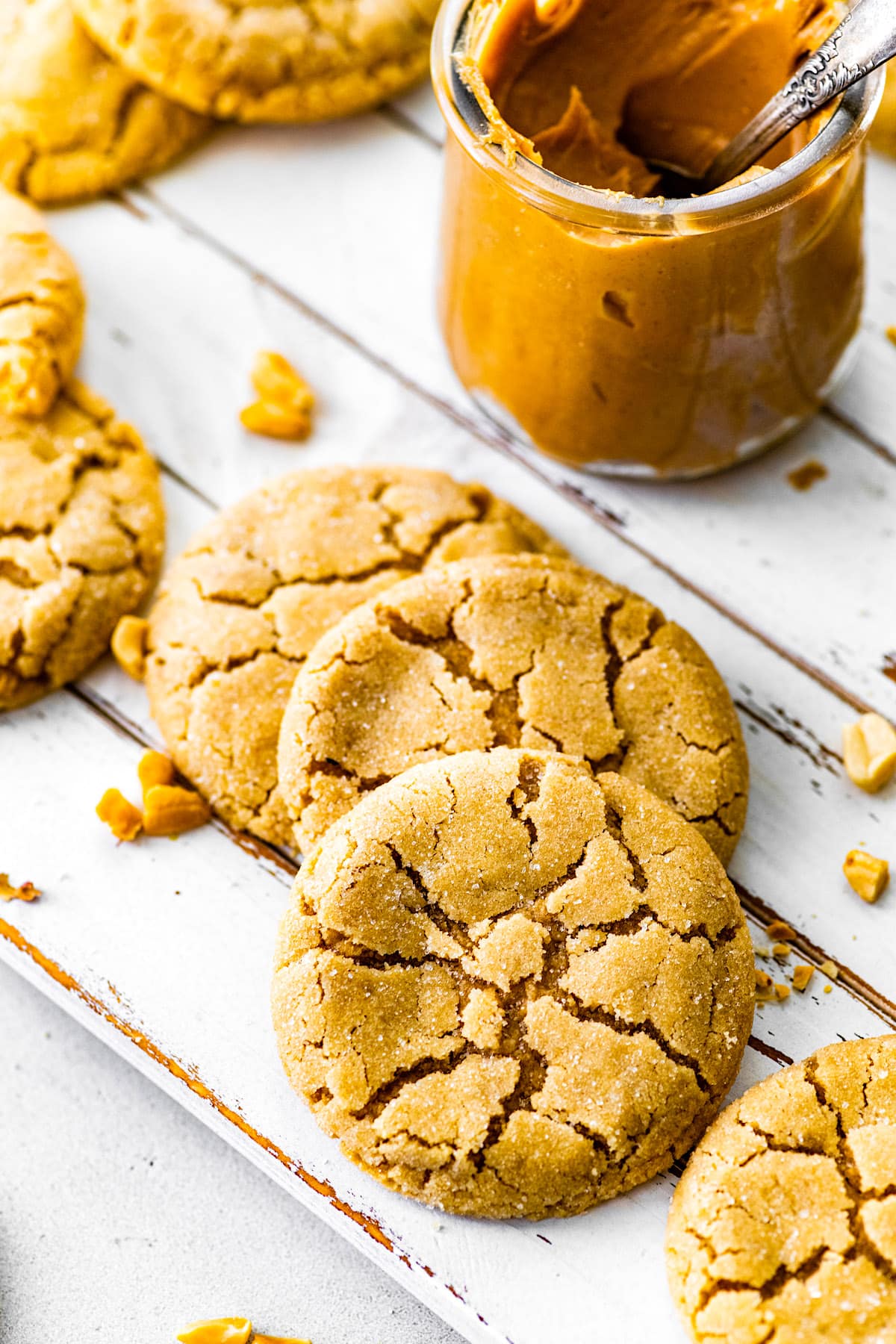 peanut butter cookies on white board with jar or peanut butter and a few peanuts. 