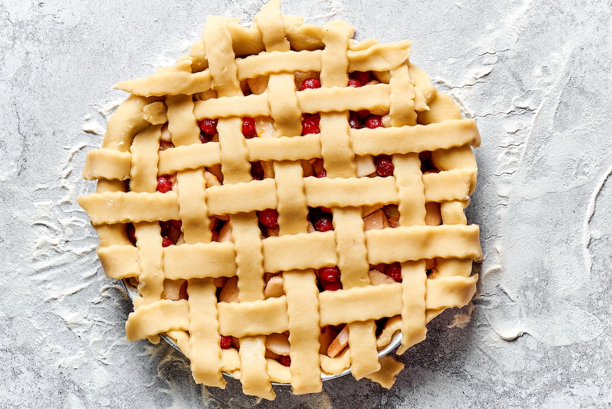 lattice woven unbaked apple cranberry pie in pie dish. 