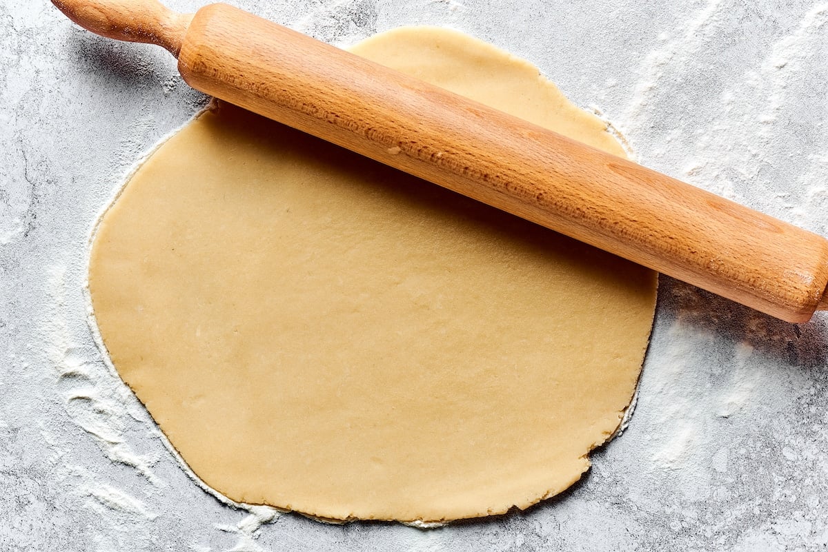 pie dough being rolled out on a lightly floured surface with a rolling pin.