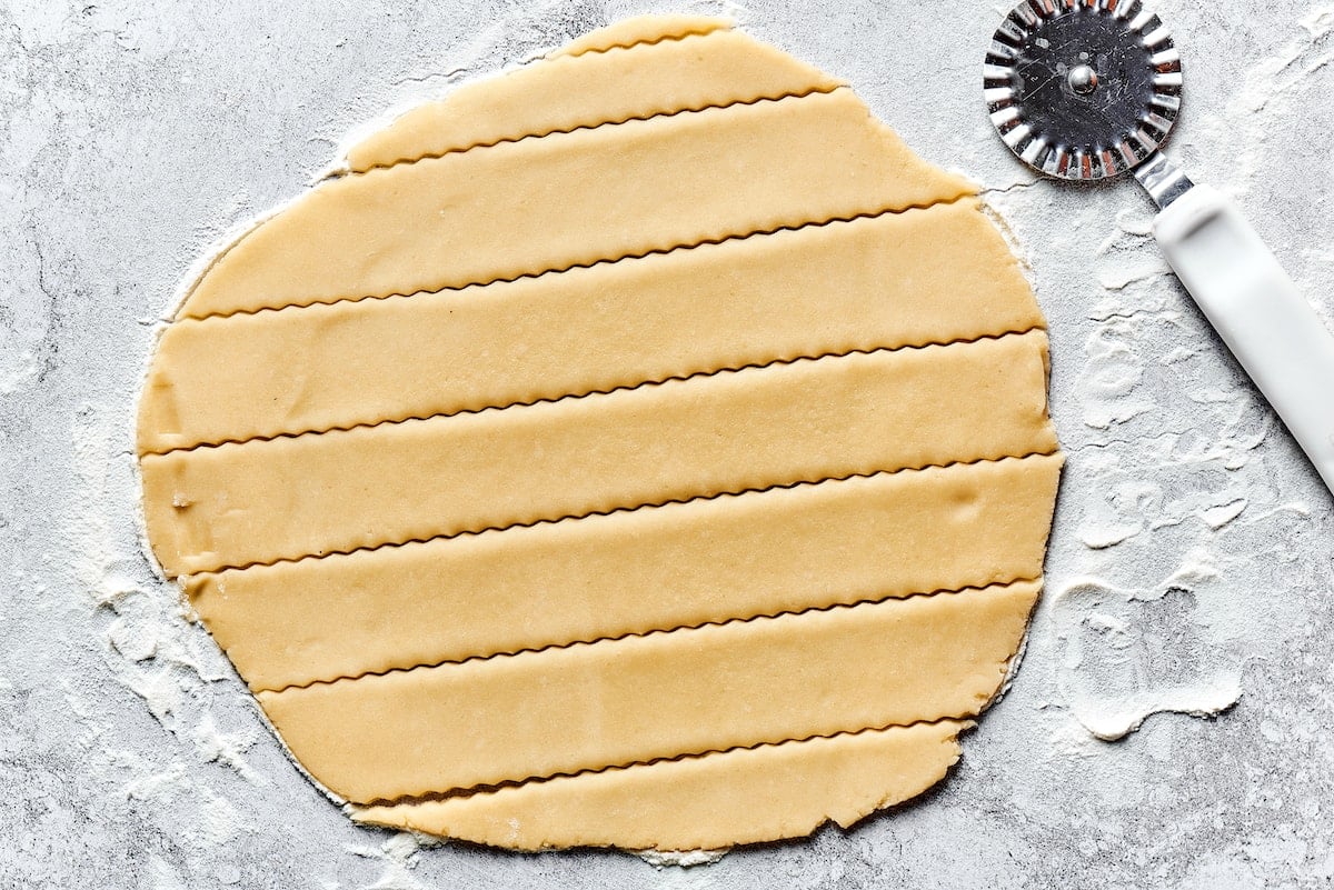 pie dough rolled out on floured surface and cut into strips with pastry cutter.