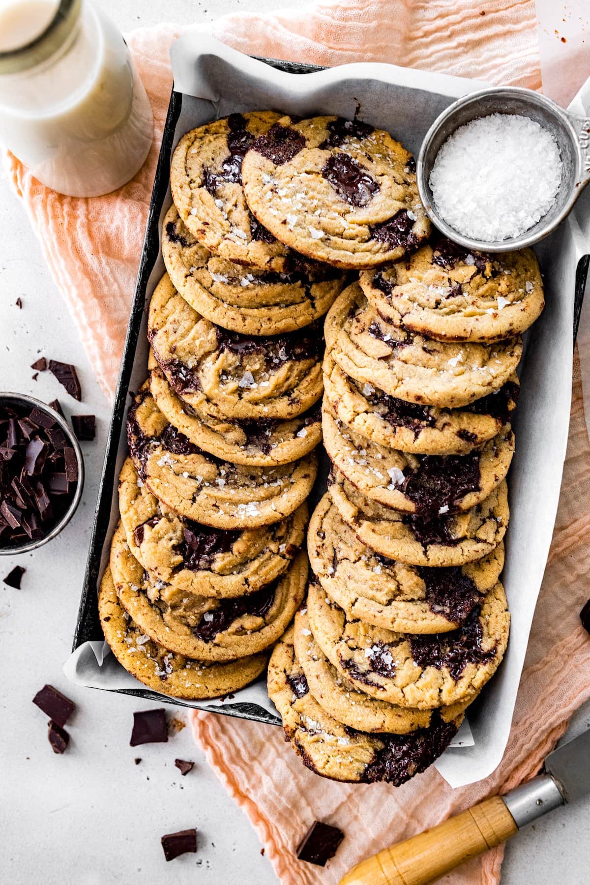 brown butter chocolate chip cookies with flaky sea salt in pan with parchment paper and bottle of milk. 