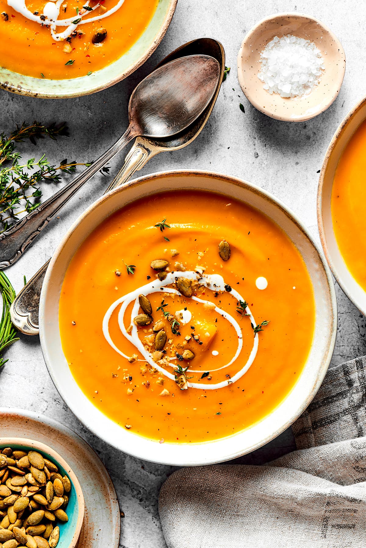 butternut squash soup in bowl with a drizzle of cream and pepitas and two spoons. 