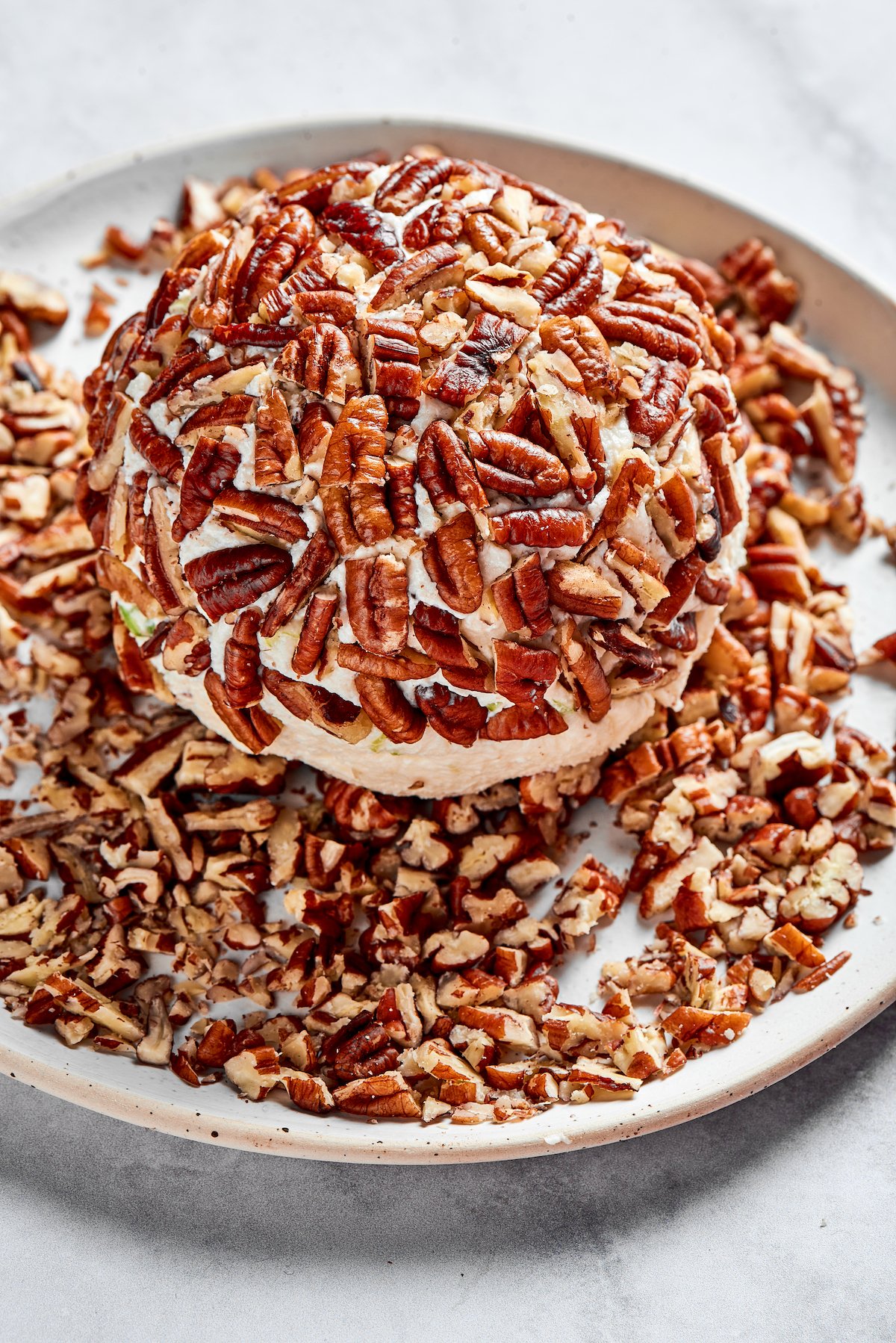 cheese ball covered in chopped pecans on plate. 