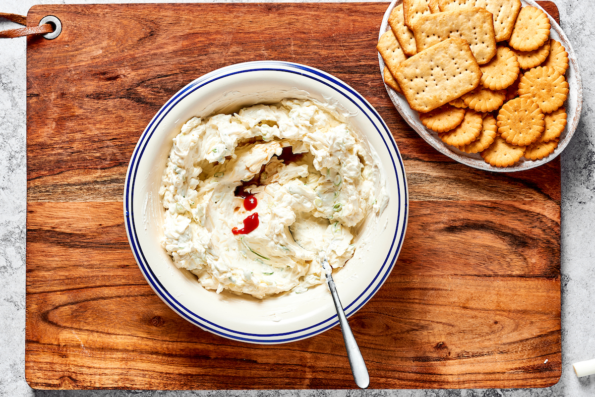 cheese ball mixture in bowl with spoon with a plate of crackers on the side. 