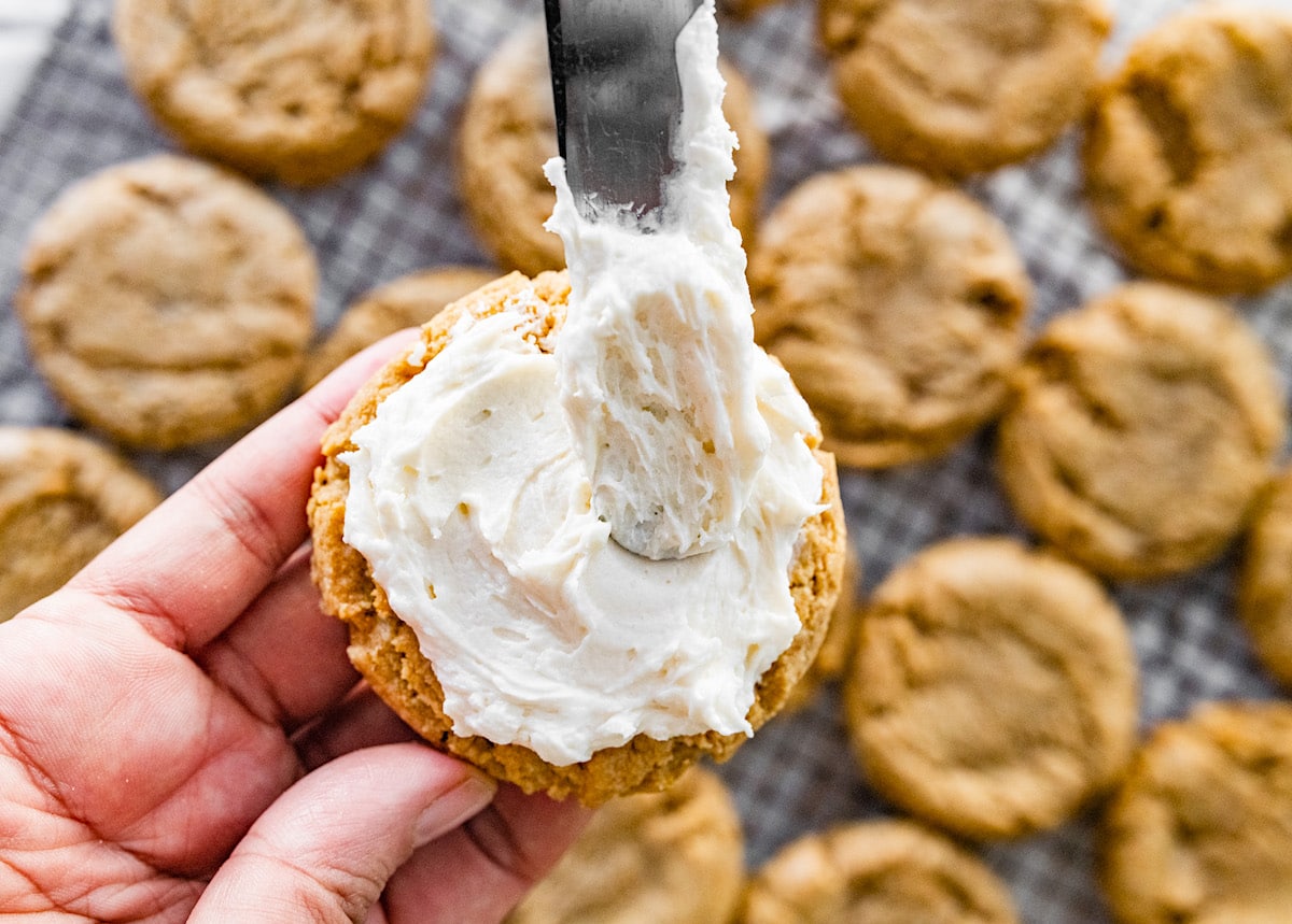 vanilla buttercream frosting being spread with a knife on graham cracker cookie. 