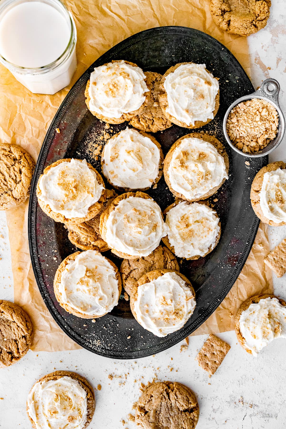 graham cracker cookies with frosting on platter with graham cracker crumbs and glass of milk.