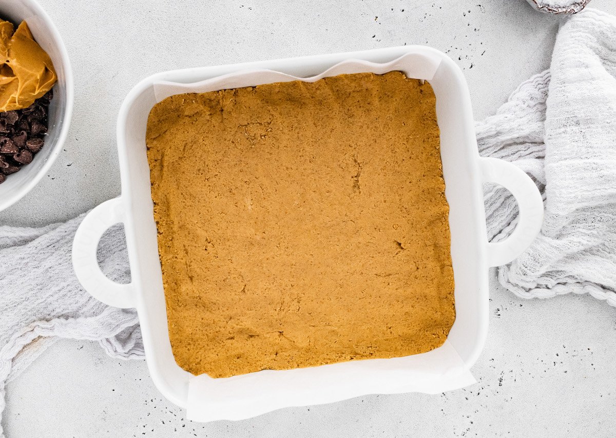 no bake peanut butter bar base pressed in baking dish with parchment paper. 