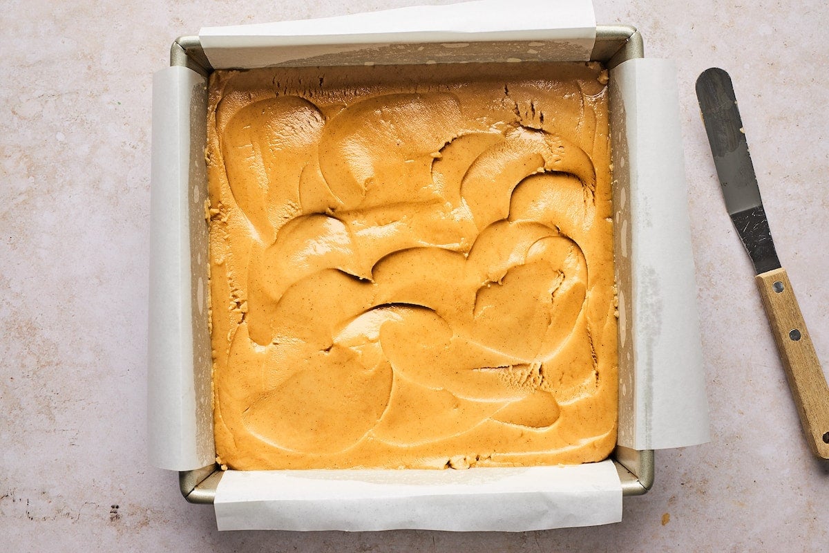 peanut butter fudge pressed in pan with parchment paper. 