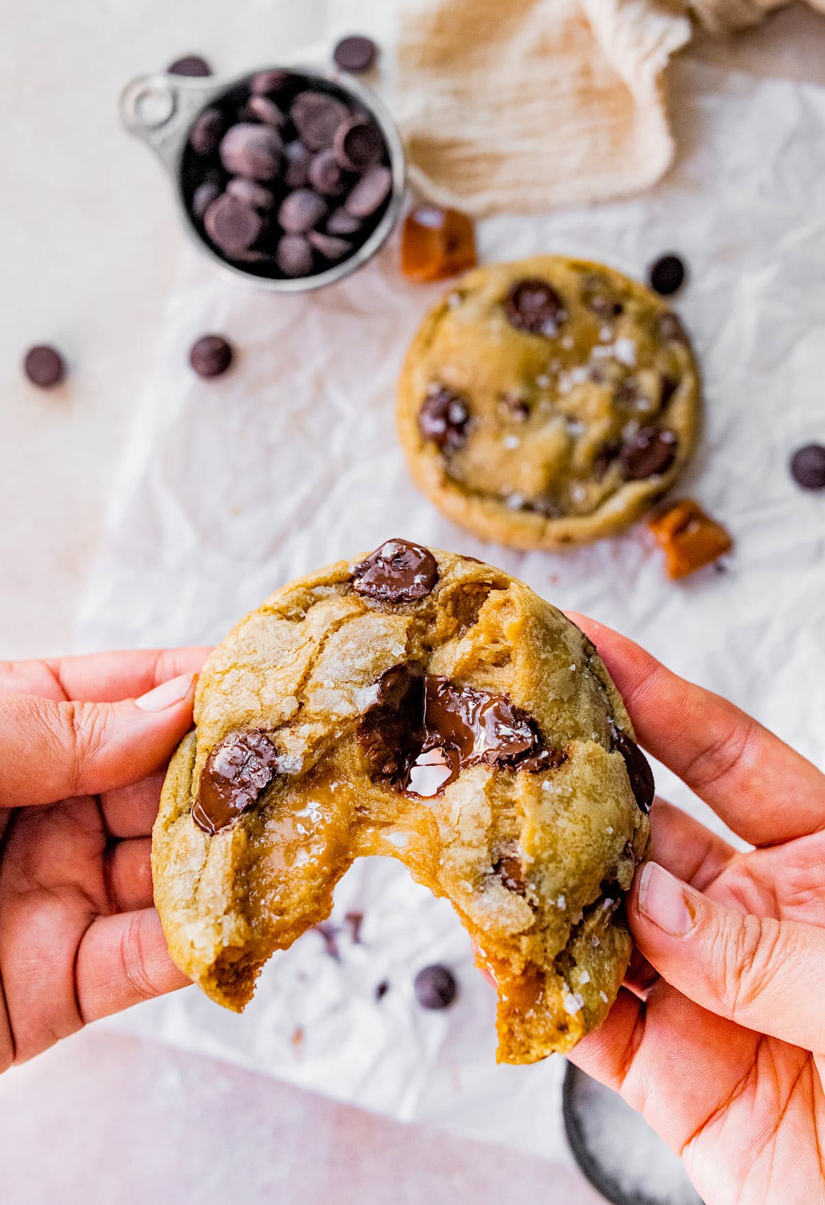 salted caramel chocolate chip cookie being broken half with a gooey caramel center. 