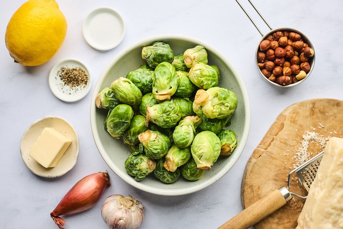 Brussels sprouts in a bowl with hazelnuts, lemon, Parmesan cheese, shallot, garlic, and butter. 