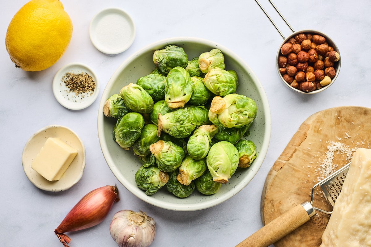 Brussels sprouts in a bowl with hazelnuts, lemon, Parmesan cheese, shallot, garlic, and butter.