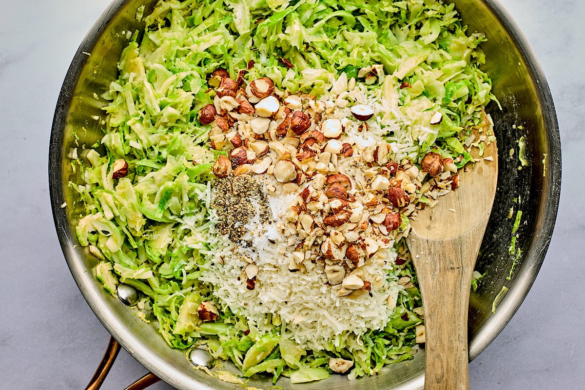shredded Brussels sprouts in pan with hazelnuts and Parmesan cheese and spoon.