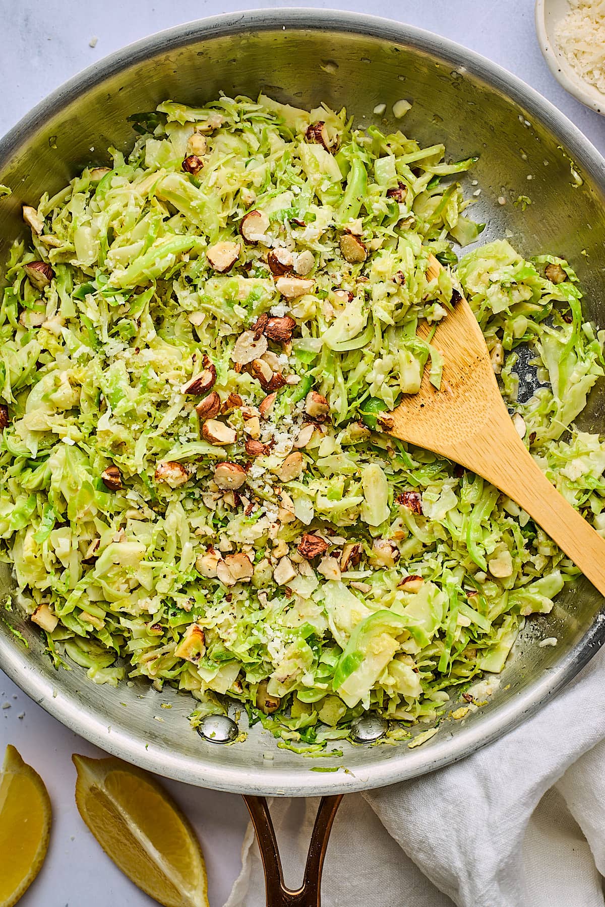 sautéed shredded Brussels sprouts in pan with hazelnuts and Parmesan cheese and wood spoon. 