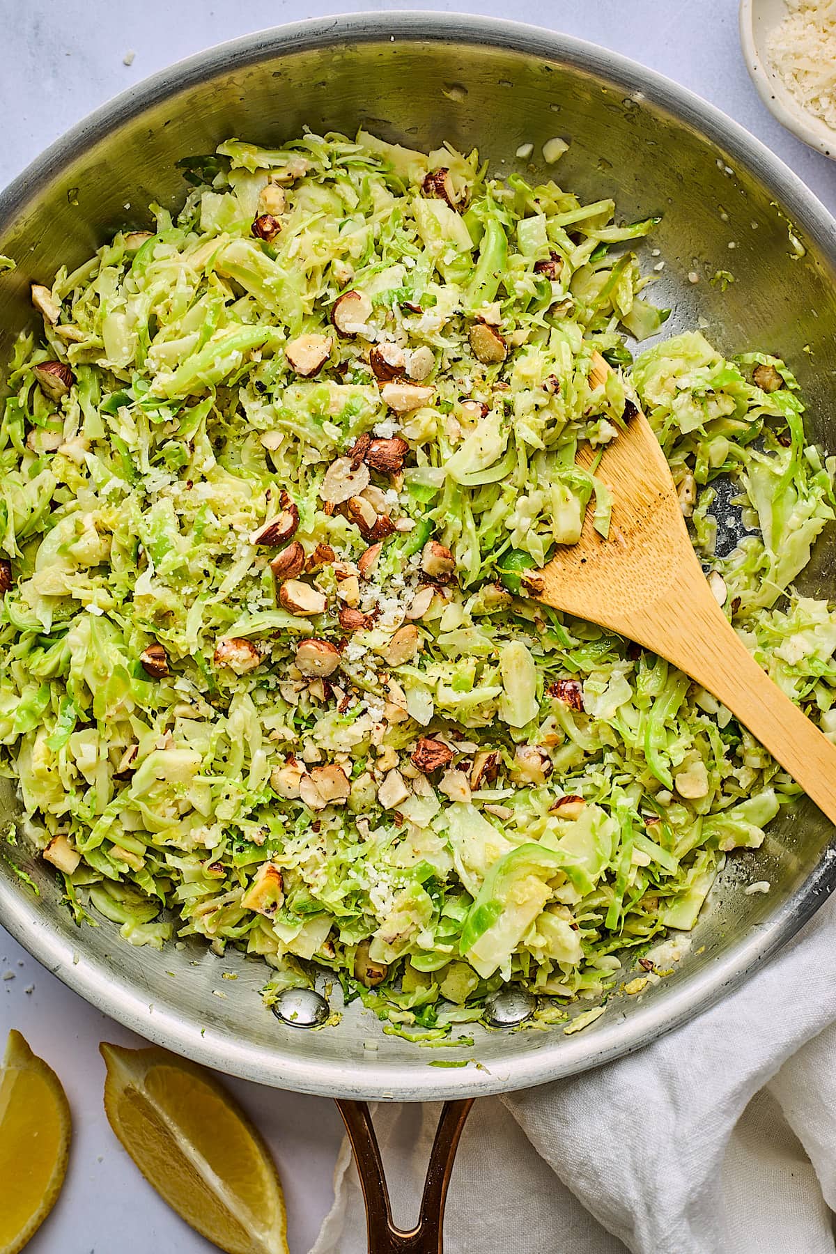 sautéed shredded Brussels sprouts in pan with hazelnuts and Parmesan cheese and wood spoon.