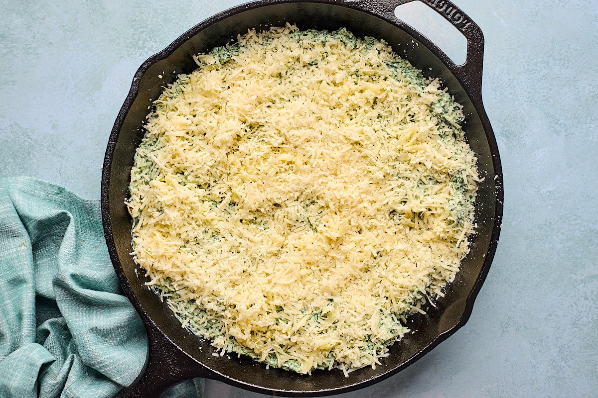 spinach artichoke dip in cast iron skillet topped with parmesan cheese ready for the oven.