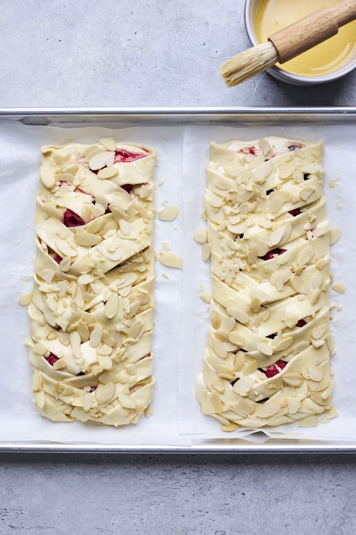 raspberry cream cheese breakfast braids on baking sheet with parchment paper topped with sliced almonds ready to be baked.