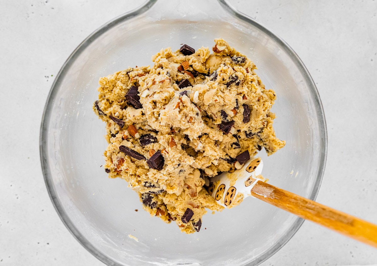 almond chocolate chip cookie dough in mixing bowl with spatula. 