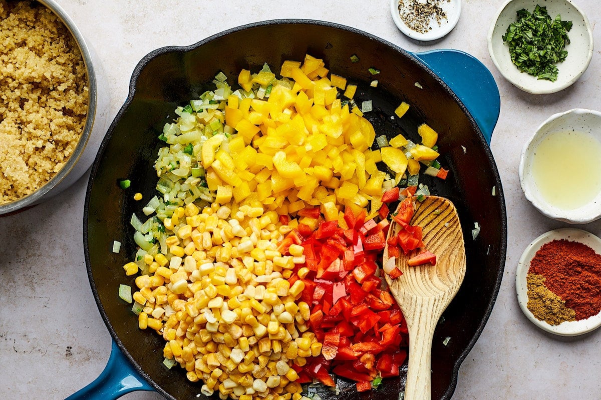 bell peppers, corn, and onion cooking in cast iron skillet with wooden spoon. 