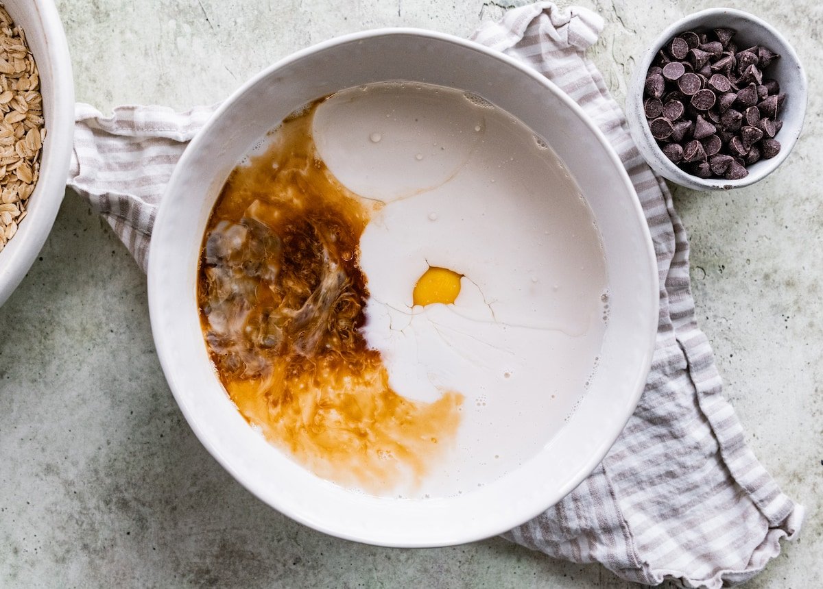 liquid ingredients in mixing bowl with tea towel and small bowl of chocolate chips.