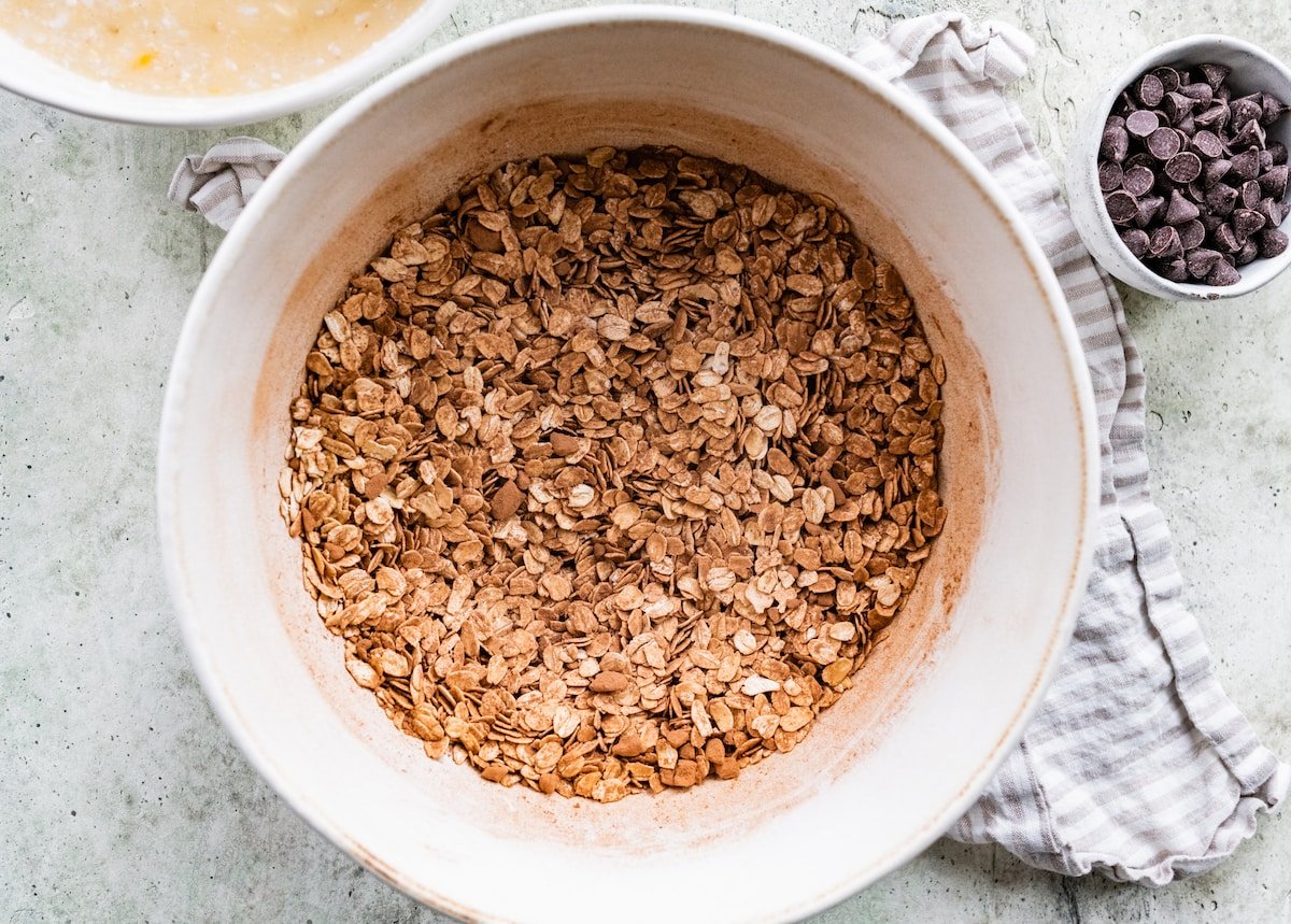 oatmeal with cocoa powder in mixing bowl with tea towel and small bowl of chocolate chips.