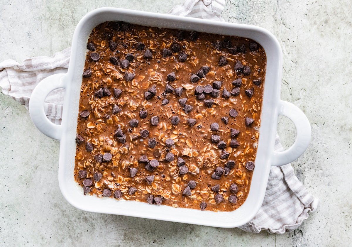 chocolate banana baked oatmeal mixture in baking pan topped with chocolate chips. 