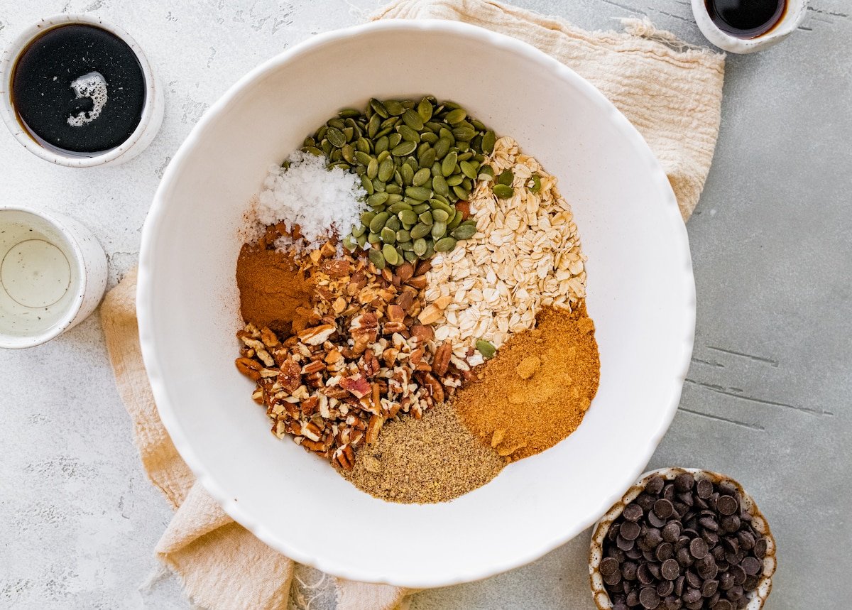 oats, cinnamon, coconut sugar, flaxseed, pecans, salt, and pepitas in large white bowl. 